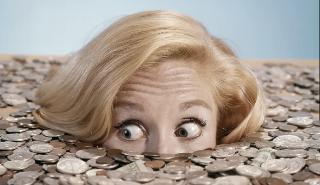 A woman peeking up from behind a mountain of coins