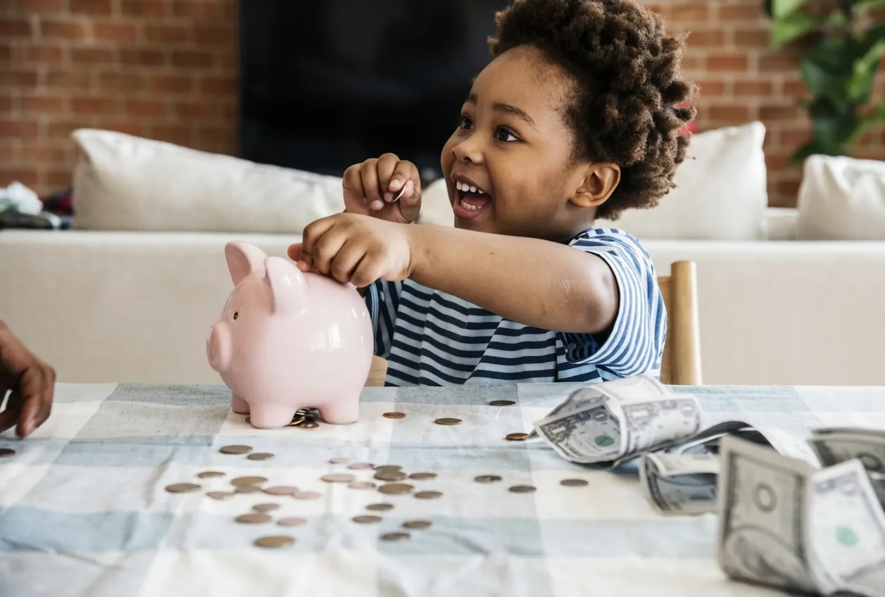A mother and young son smiling as they put coins into a pink piggy bank